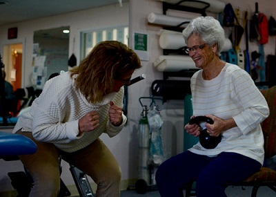 Female Physical Therapist working with an elderly female who is lifting a ball weight